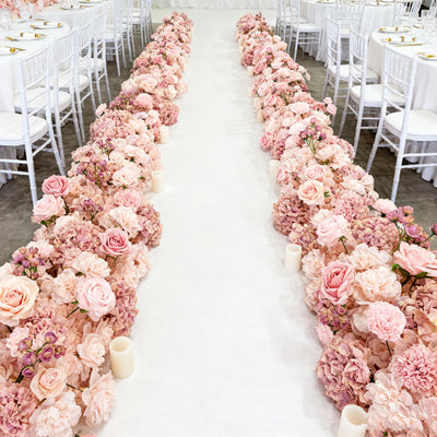 Elegant floral arrangement lining a wedding aisle with candles and chairs.