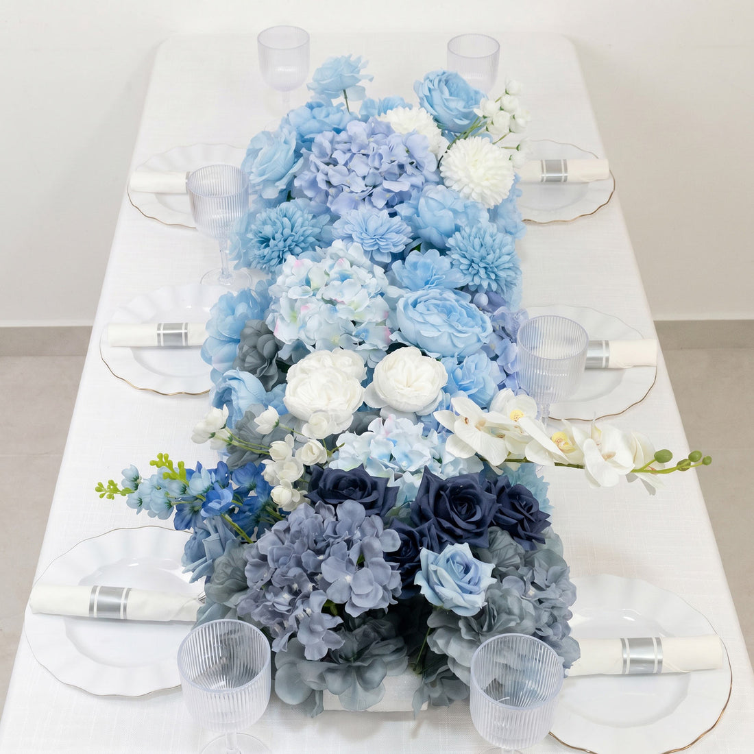 Blue floral table runner with white plates and clear ribbed glasses on a dining table
