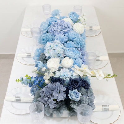 Blue floral table runner with white plates and clear ribbed glasses on a dining table