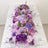 Purple floral table centerpiece with elegant glassware and plates.