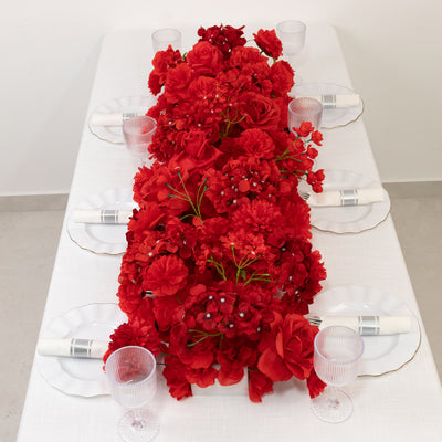 Red floral table runner with white plates and clear glasses on a dining table.