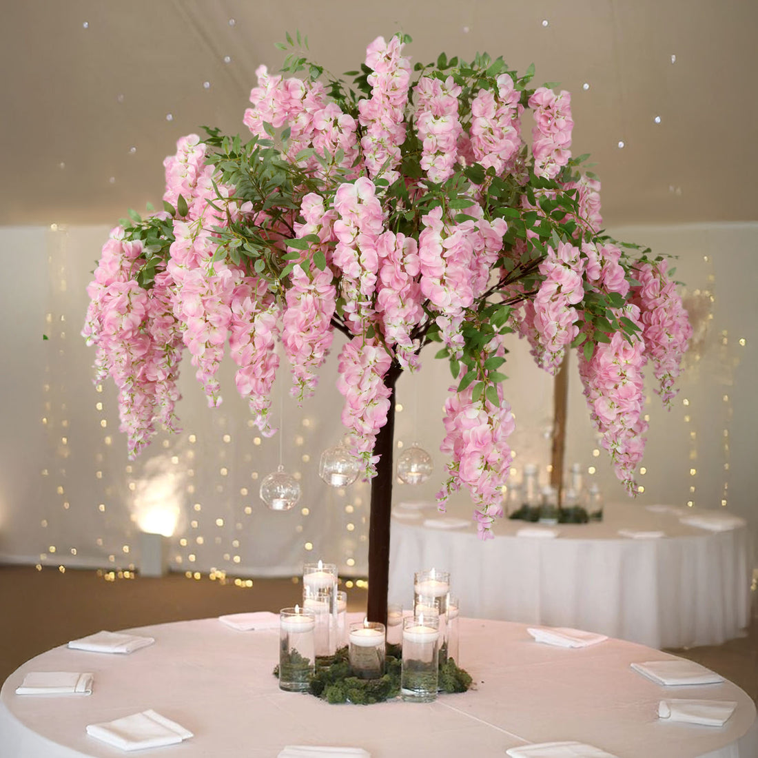 Artificial pink wisteria tree centerpiece with candles on a round table.