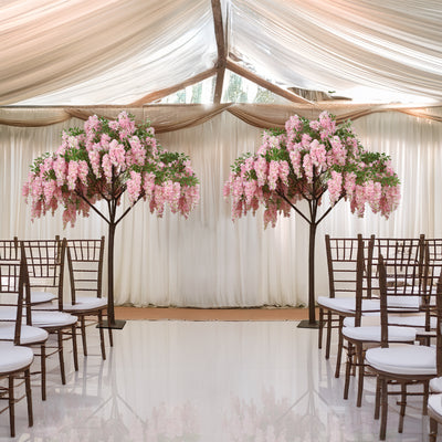 Elegant wedding setup with pink wisteria trees and white chairs under draped fabric.