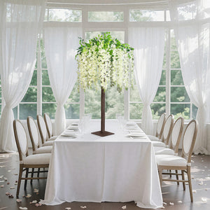 Elegant floral centerpiece on a dining table with white drapes and soft lighting.