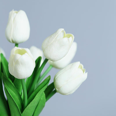 White tulip bouquet with green leaves against a soft gray background.