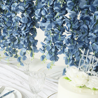 Blue floral arrangement draping over a table setting with cake and glassware.
