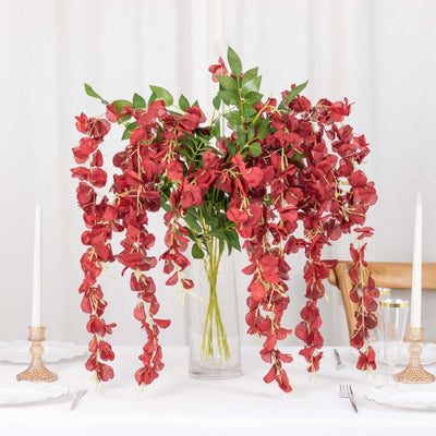 Red floral arrangement in a clear vase with cascading blooms on a dining table.