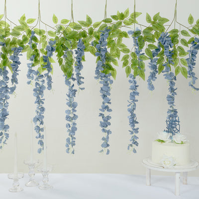 Blue floral garland with greenery hanging above a wedding cake and candles.
