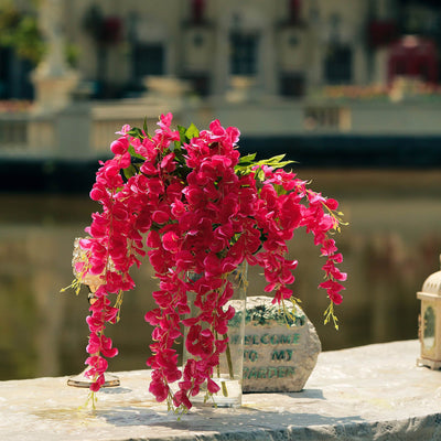 Pink cascading flowers in a vase by a serene water backdrop.