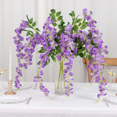 Purple floral arrangement in a clear vase on a dining table.