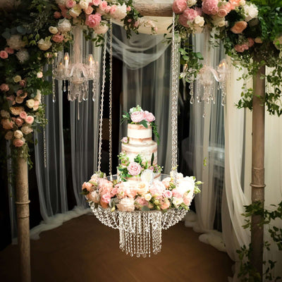 Elegant wedding cake adorned with flowers and crystals, suspended in a floral arch.