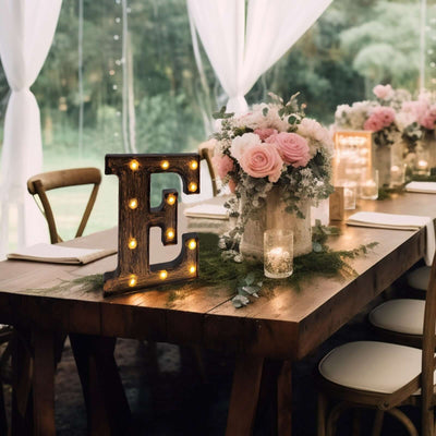 Rustic illuminated letter 'E' on a wooden table with floral centerpiece.