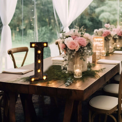 Rustic table setting with flowers and illuminated letter in a decorative arrangement.