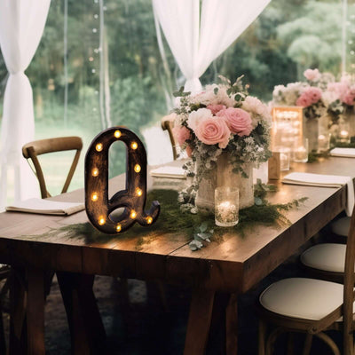 Decorative marquee letter "q" with lights on a rustic table with flowers and candles.