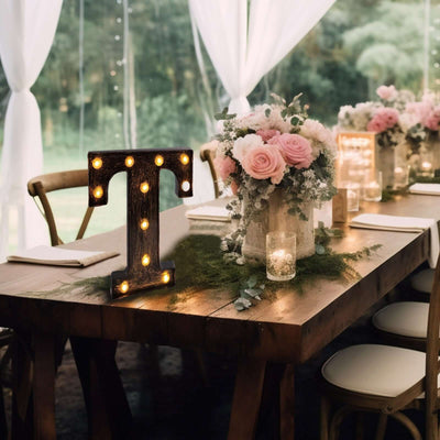 Decorative light-up letter 'T' on a rustic table with floral centerpiece.