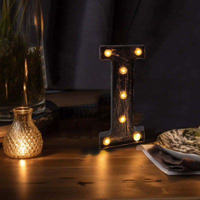 Decorative wooden letter "I" with lights, illuminated on a table.