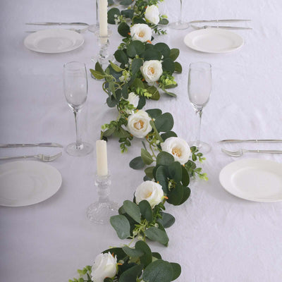 Elegant floral table runner with white roses and greenery on a dining table.