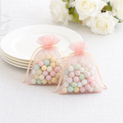 Pastel candy balls in pink organza gift bags on a white table
