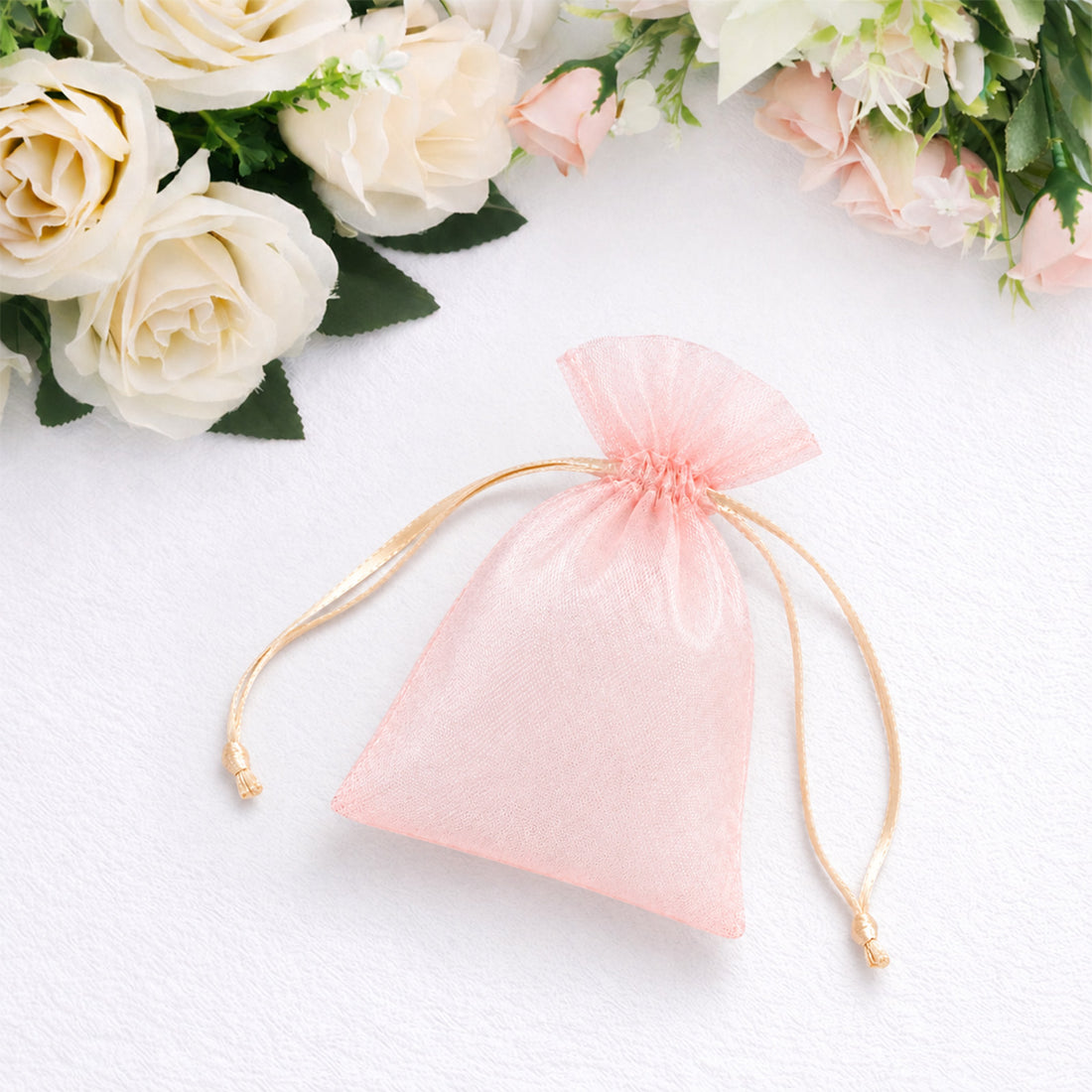 Pink organza drawstring gift bag with white roses on soft white background