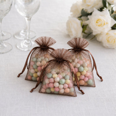 Brown organza candy favor bags with pastel sweets on a white table