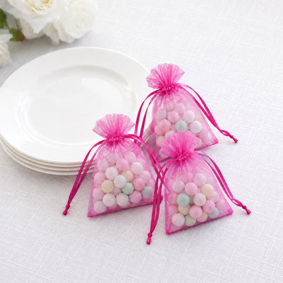 Pink organza gift bags with pastel candies beside white plates