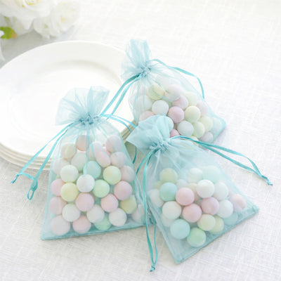 Pastel candy-filled organza bags on a table with white plates.