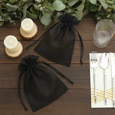 Black organza gift bags on a wooden table with candles and utensils.