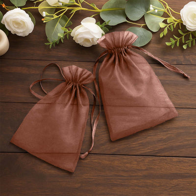 Brown organza gift bags on a wooden surface with decorative flowers.