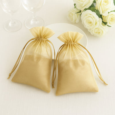 Two gold organza bags tied with ribbon on a table with roses in the background.