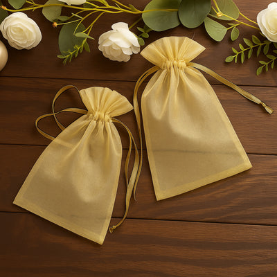 Two sheer yellow drawstring gift bags on a wooden surface with floral accents.
