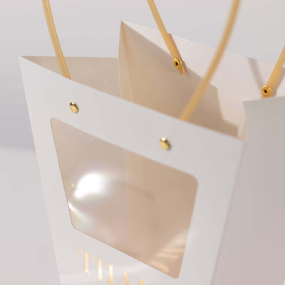 White gift bag with transparent window and golden accents.