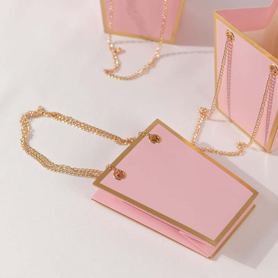 Pink handbag with gold accents and chain strap on a light background.