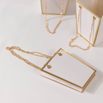 Elegant blank gift tags with gold accents and chains on a white backdrop.