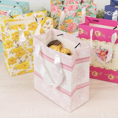 Colorful decorative gift bags with chocolates inside on a light surface.