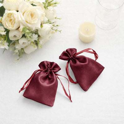 Two burgundy satin drawstring bags on a textured white surface.