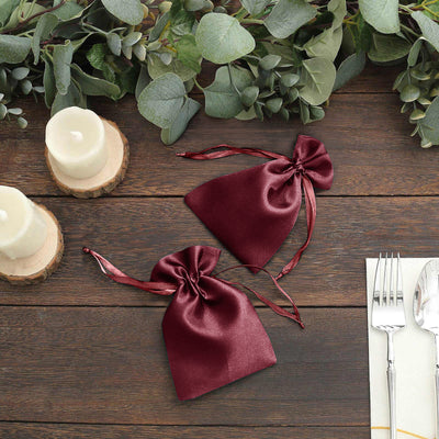 Burgundy satin drawstring bags on a rustic wooden table with greenery