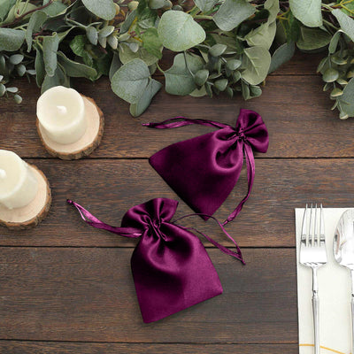 Purple satin drawstring bags on a wooden table with greenery and candles.