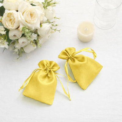 Yellow satin drawstring bags with floral arrangement and candle in the background.
