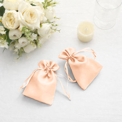 Peach satin drawstring bags beside a bouquet and candle