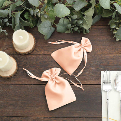 Peach satin drawstring bags on a wooden table with greenery and candles.