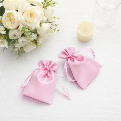 Pink satin drawstring bags beside a bouquet of roses and a candle.