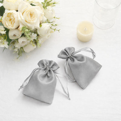 Gray satin drawstring bags with floral arrangement and candle.