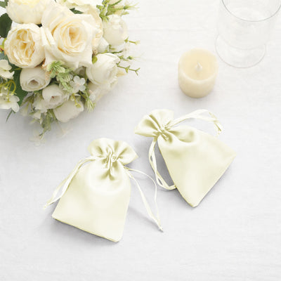 Two elegant silk favor bags in soft yellow, styled with ribbons and placed near white flowers.