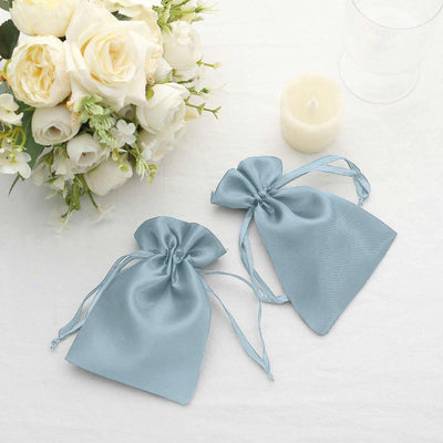 Blue satin drawstring bags styled with a bouquet and candle on a table.