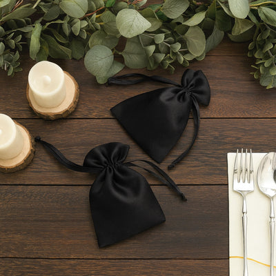 Black satin favor bags styled with candles and greenery on a wooden table.