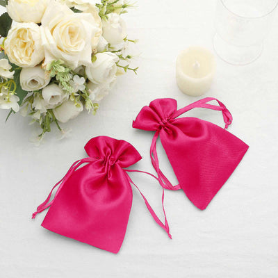 Pink satin gift bags with drawstrings, styled with floral arrangement and candle.