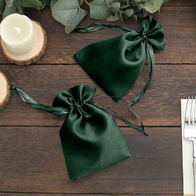 Dark green satin drawstring bags on a wooden table.