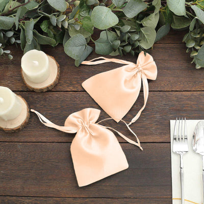 Two elegant satin drawstring bags on a wooden table with greenery and candles.
