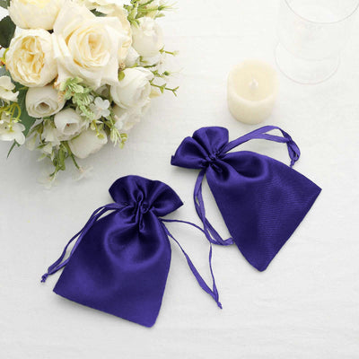Two purple satin gift bags displayed with white roses and a candle.