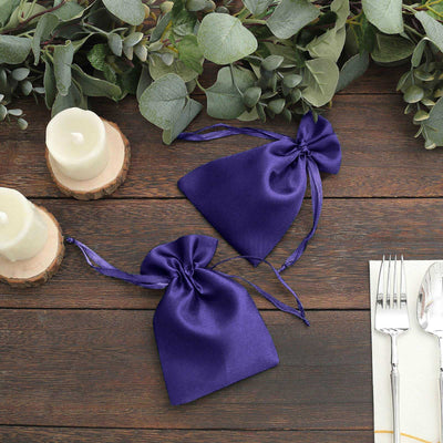Purple satin drawstring bags on a rustic wooden table with greenery and candles.